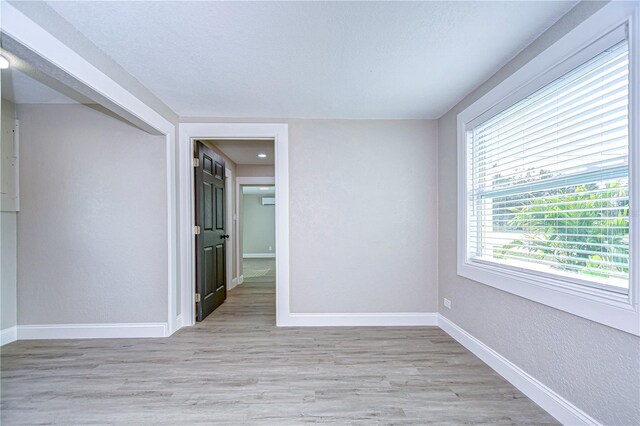 spare room with light wood finished floors, baseboards, a textured ceiling, and a textured wall