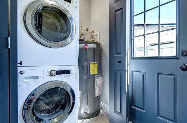 washroom featuring stacked washer and dryer, water heater, laundry area, and a textured wall