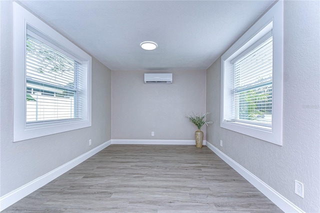 empty room featuring a textured wall, light wood-style flooring, baseboards, and a wall mounted air conditioner