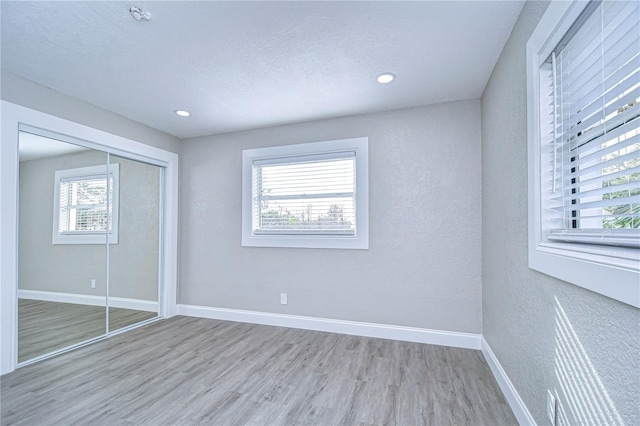 unfurnished bedroom with light wood-type flooring, a closet, a textured ceiling, and baseboards