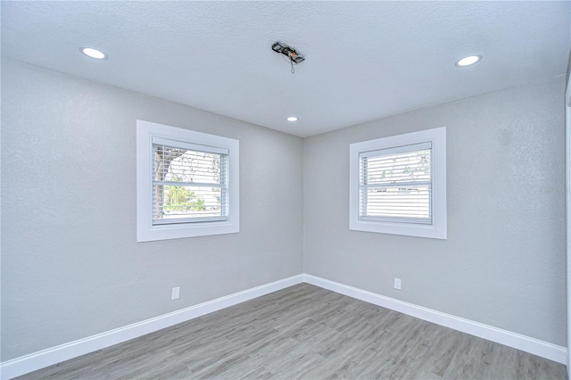 unfurnished room with a textured ceiling, recessed lighting, light wood-style flooring, and baseboards