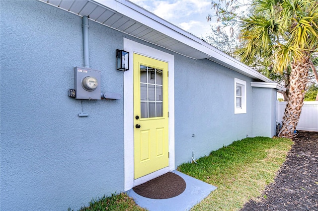 view of exterior entry with fence and stucco siding