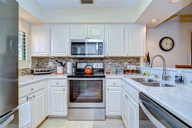 kitchen featuring appliances with stainless steel finishes, sink, white cabinets, backsplash, and light stone countertops