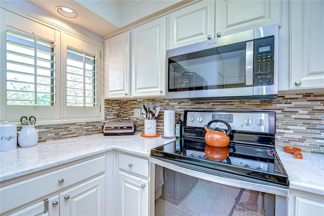 kitchen with decorative backsplash, white cabinets, and appliances with stainless steel finishes