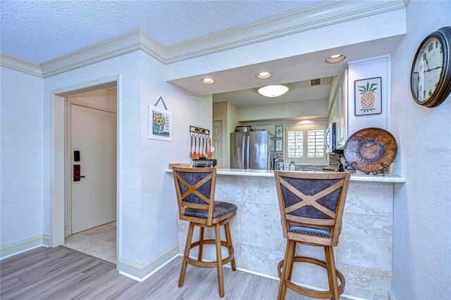 kitchen with a kitchen bar, a textured ceiling, stainless steel fridge, kitchen peninsula, and light hardwood / wood-style floors