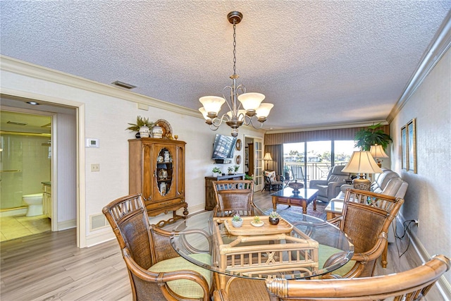 dining room featuring an inviting chandelier, crown molding, light hardwood / wood-style floors, and a textured ceiling