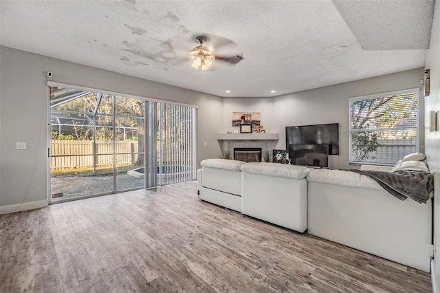 living room with hardwood / wood-style flooring, ceiling fan, a tile fireplace, and a textured ceiling