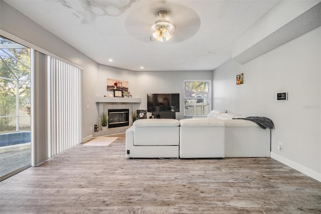 living room with ceiling fan, a tile fireplace, and light wood-type flooring