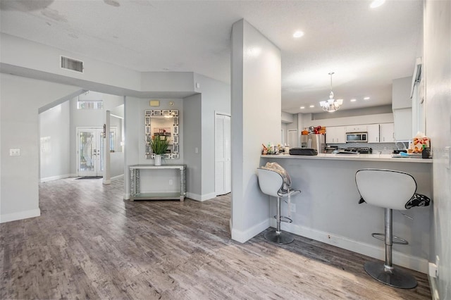 kitchen featuring pendant lighting, appliances with stainless steel finishes, white cabinetry, wood-type flooring, and kitchen peninsula