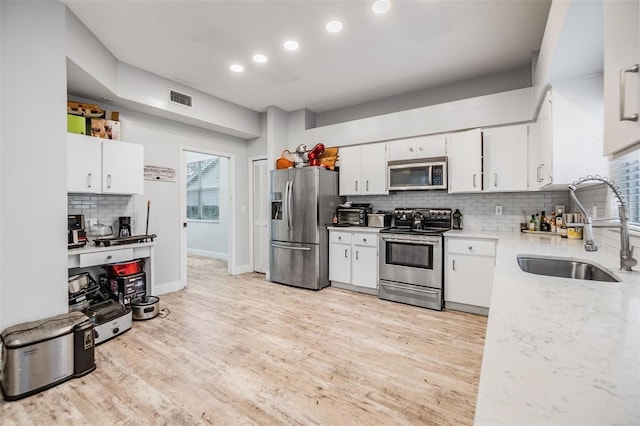 kitchen with stainless steel appliances, white cabinetry, sink, and light wood-type flooring