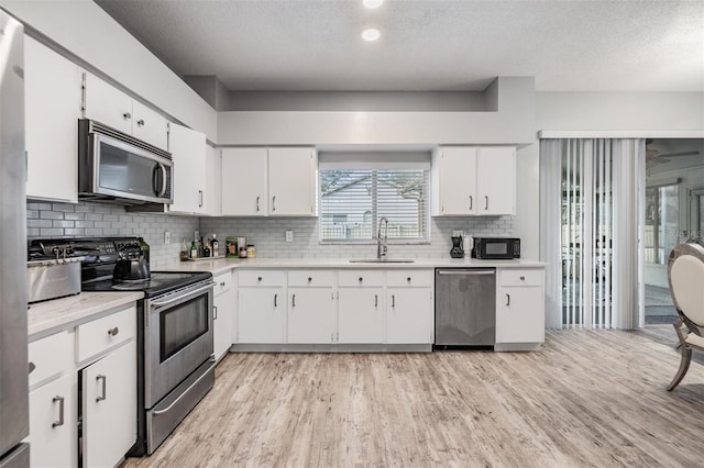 kitchen featuring sink, light hardwood / wood-style flooring, white cabinetry, stainless steel appliances, and tasteful backsplash