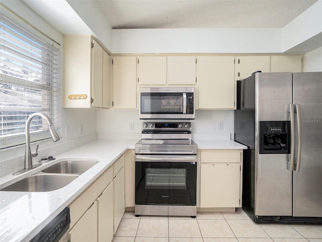 kitchen featuring appliances with stainless steel finishes, sink, light tile patterned floors, cream cabinets, and a textured ceiling