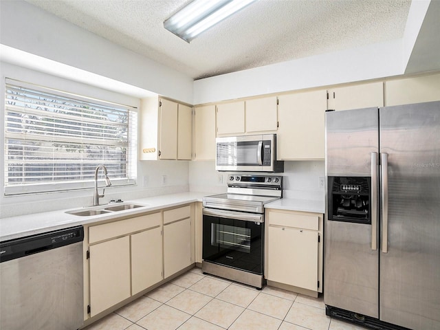 kitchen with light tile patterned flooring, appliances with stainless steel finishes, sink, a textured ceiling, and cream cabinetry