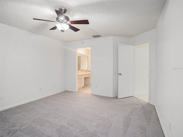 unfurnished bedroom featuring ceiling fan, light colored carpet, a textured ceiling, and ensuite bath