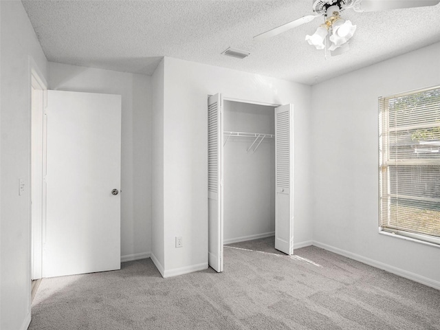 unfurnished bedroom with a textured ceiling, light colored carpet, a closet, and ceiling fan