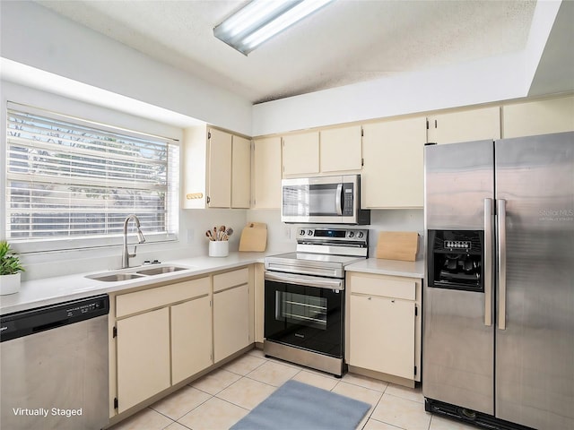 kitchen featuring appliances with stainless steel finishes, sink, light tile patterned floors, cream cabinets, and a textured ceiling