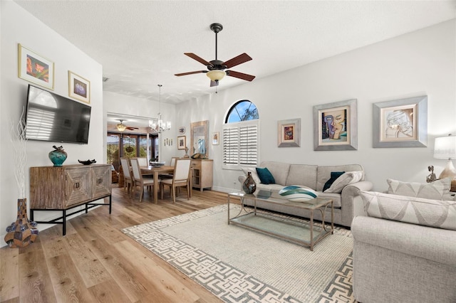 living room featuring ceiling fan with notable chandelier, light hardwood / wood-style flooring, and a textured ceiling