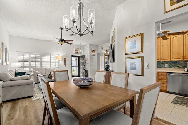 dining space featuring light wood-type flooring, ceiling fan with notable chandelier, and a textured ceiling