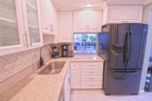 kitchen featuring sink, light tile patterned floors, fridge, light stone countertops, and white cabinets