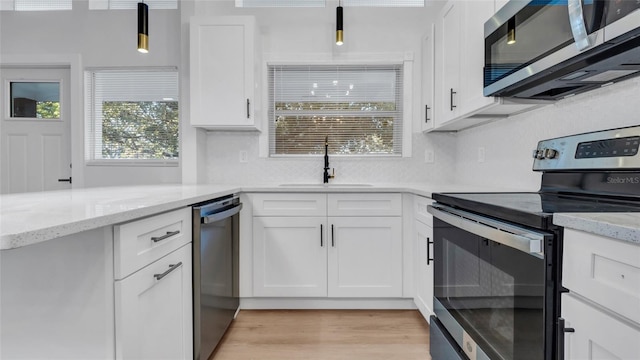 kitchen with sink, appliances with stainless steel finishes, pendant lighting, light stone countertops, and white cabinets