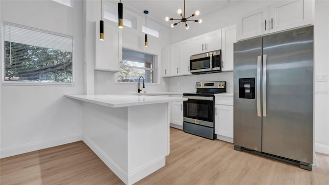 kitchen with pendant lighting, appliances with stainless steel finishes, kitchen peninsula, and white cabinets