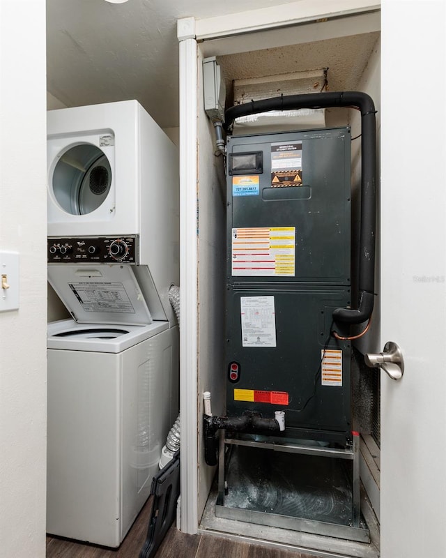 clothes washing area with stacked washing maching and dryer and heating unit