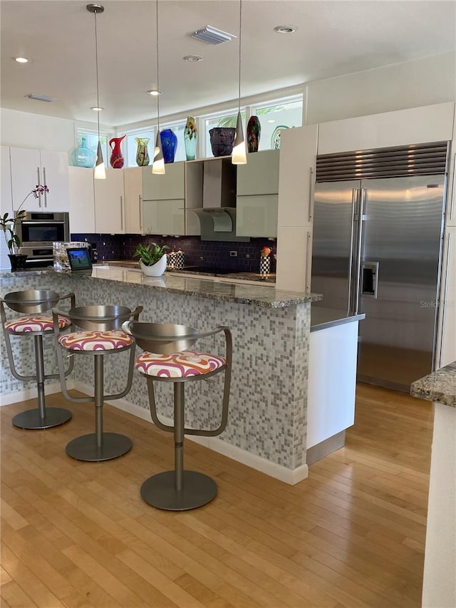 kitchen featuring stainless steel built in refrigerator, light hardwood / wood-style flooring, hanging light fixtures, and white cabinets