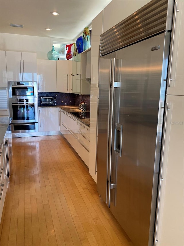 kitchen featuring decorative backsplash, stainless steel appliances, white cabinets, and light wood-type flooring