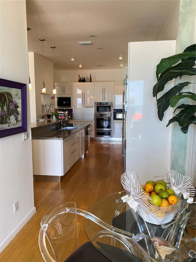 kitchen featuring built in microwave, hardwood / wood-style flooring, hanging light fixtures, and white cabinets