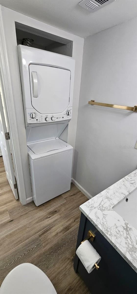 bathroom featuring vanity, hardwood / wood-style floors, stacked washer and clothes dryer, and toilet