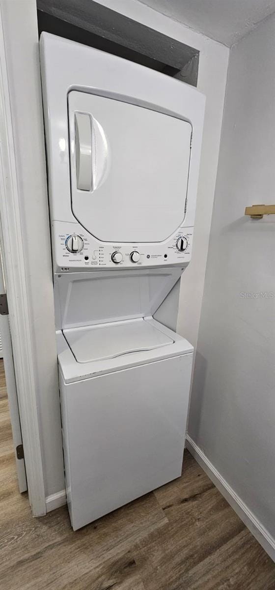 laundry room featuring stacked washer / dryer and wood-type flooring