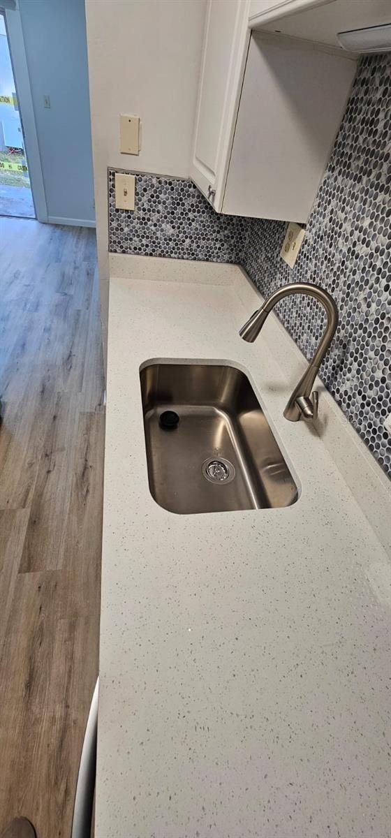 room details with white cabinetry, sink, tasteful backsplash, and light wood-type flooring