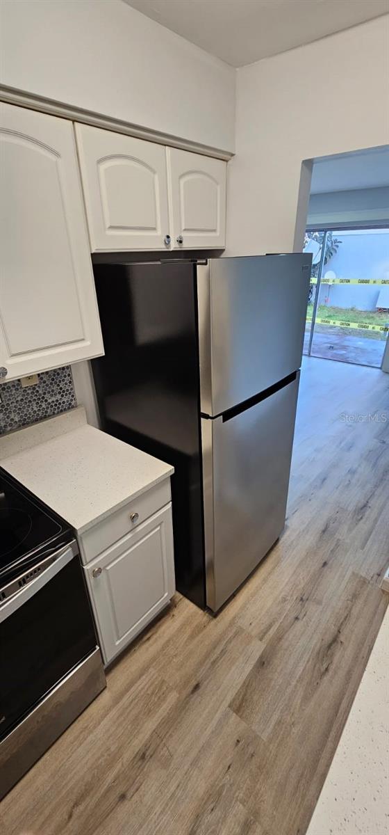 kitchen with stainless steel appliances, white cabinetry, and light hardwood / wood-style flooring