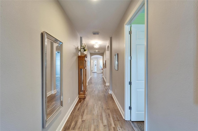 corridor featuring light wood-style floors, baseboards, visible vents, and arched walkways