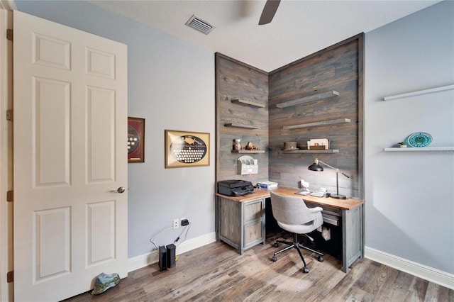 home office with wooden walls, wood finished floors, a ceiling fan, visible vents, and baseboards