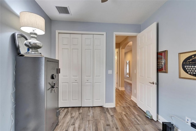 bedroom with light wood-type flooring, arched walkways, visible vents, and baseboards