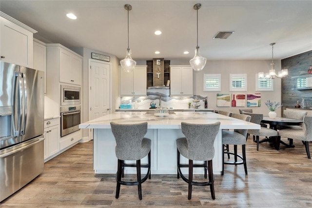 kitchen with wall chimney exhaust hood, visible vents, white cabinetry, and stainless steel appliances