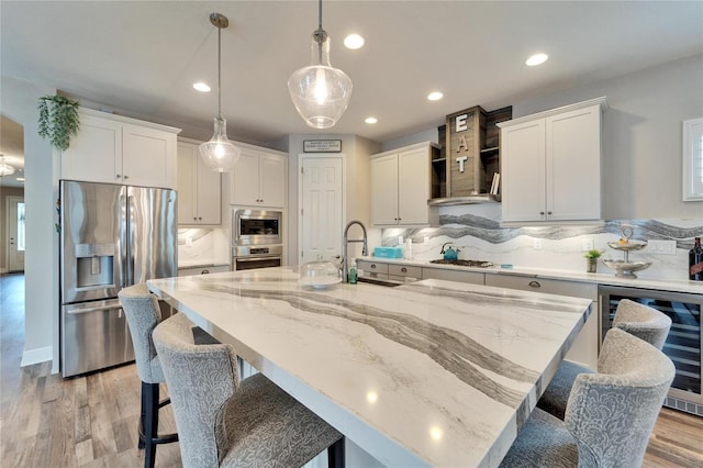 kitchen with wine cooler, decorative light fixtures, a center island with sink, stainless steel appliances, and white cabinets