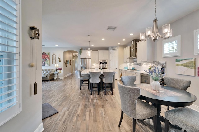 dining room with arched walkways, wine cooler, recessed lighting, visible vents, and light wood finished floors