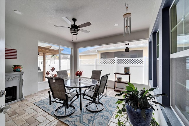 dining space with brick floor, ceiling fan, an outdoor fireplace, and a textured ceiling