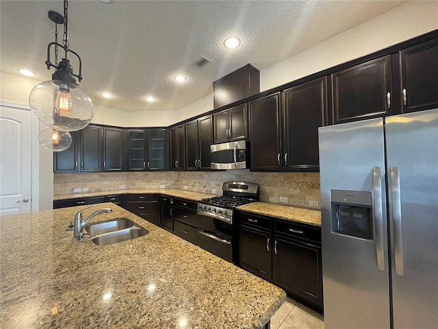 kitchen with light stone counters, appliances with stainless steel finishes, decorative light fixtures, and sink