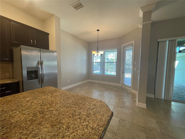 kitchen featuring stainless steel refrigerator with ice dispenser, light tile patterned flooring, an inviting chandelier, dark brown cabinets, and light stone countertops