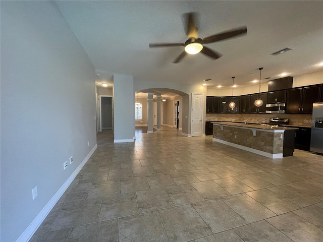 kitchen with a breakfast bar, decorative light fixtures, a center island with sink, appliances with stainless steel finishes, and backsplash