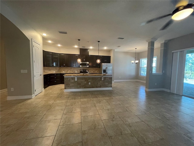 kitchen featuring hanging light fixtures, stainless steel appliances, tasteful backsplash, an island with sink, and ceiling fan with notable chandelier