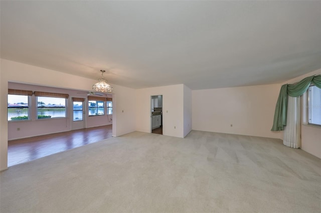 unfurnished living room featuring a water view, a chandelier, and light carpet