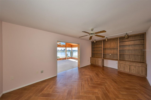 unfurnished living room with parquet floors, ceiling fan, and built in desk