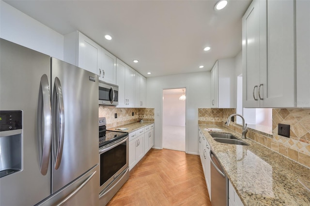 kitchen with light stone counters, light parquet floors, stainless steel appliances, and white cabinets