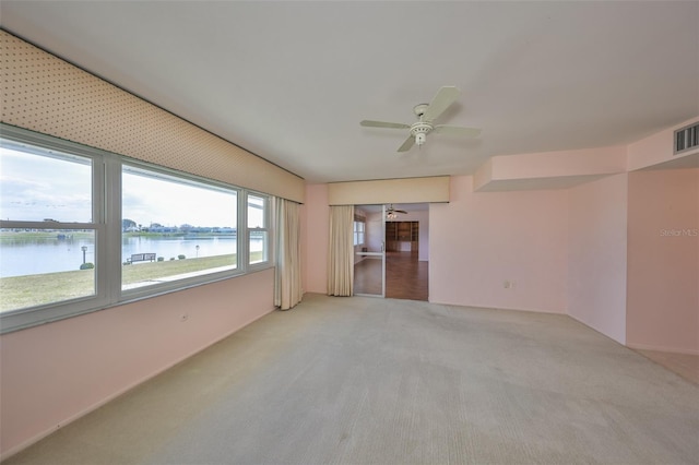 spare room with a water view, light colored carpet, and ceiling fan