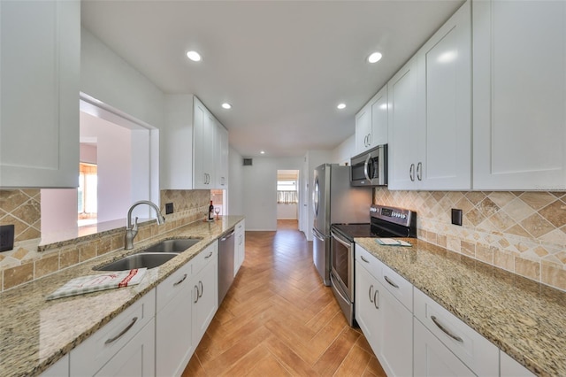 kitchen featuring sink, white cabinets, stainless steel appliances, light stone countertops, and light parquet floors