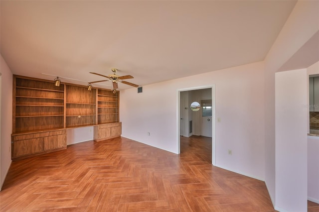 unfurnished living room with ceiling fan, parquet flooring, built in desk, and built in shelves